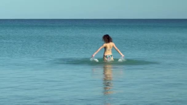 Uma jovem mulher salpicando no mar. Mulher de fato de banho no Mediterrâneo. Descansar no mar. A divertir-se na água. Temporada de natação — Vídeo de Stock