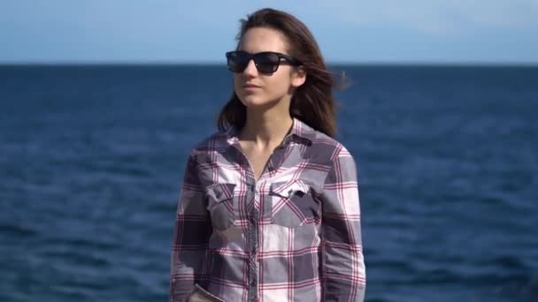 Une jeune femme sur fond de mer. Fille en lunettes de soleil par temps ensoleillé. Explore la nature environnante — Video