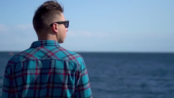한 젊은이 가 바다를 바라봅니다. 파란 셔츠를 입은 남자는 자연을 동경합니다. 카메라 에등을 대고 서 있는 남자. — 비디오
