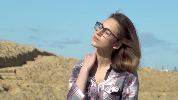 En ung kvinna sitter på stenar på en bakgrund av havet. Vinden blåser på flickans hår. Solen skiner i ansiktet. Kvinna med slutna ögon — Stockvideo