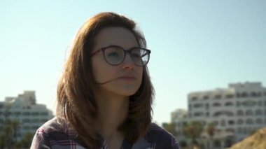Evlerin arka planında genç bir kadın. Kız rüzgarda saçlarını sallıyor. Güneş ışıl ışıl parlıyor. Yavaş çekim.