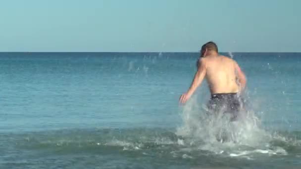 Läuft ein junger Mann ins Meer und stürzt. Ein Mann in Badehose im Mittelmeer. Ruhe auf See. Spaß im Wasser. Badesaison — Stockvideo