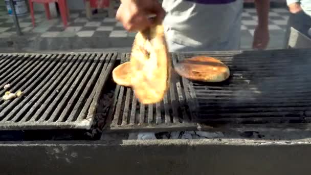 Chlebové placky jsou smažené na dřevěném uhlí. Chlap dává na gril chleba. Kouř ze smažení — Stock video