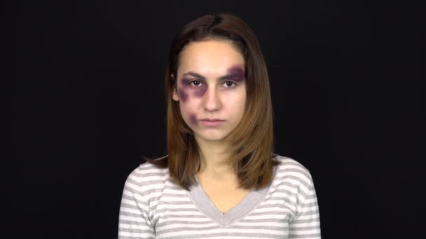 En ung kvinna tittar på kameran. En kvinna med blåmärken i ansiktet. Gräl i en ung familj. Våld i hemmet. På en svart bakgrund — Stockvideo