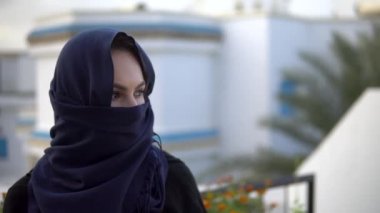Arap çarşaflı genç bir kadın. Bir kadın kameraya bakıyor. Arap evinin arka planına karşı..