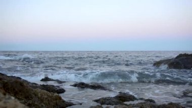 Akdeniz 'de dalgalar var. Dalgalar pembe gün batımında kayalara çarpar. Yavaş çekim