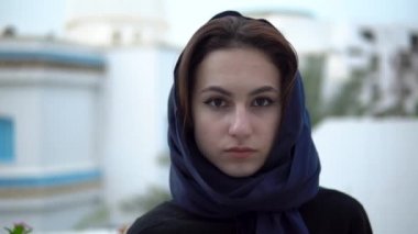 Arap başörtüsü takan genç bir kadın. Bir kadın kameraya bakıyor. Arap evinin arka planına karşı..