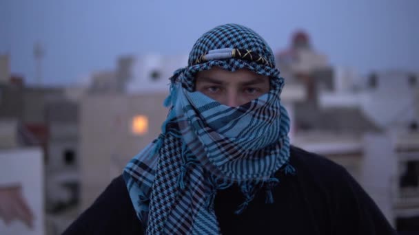 Young man in arabic handkerchief. A man looks at the camera and opens a handkerchief. On the roof of the house against the backdrop of Arab houses. — Stock Video