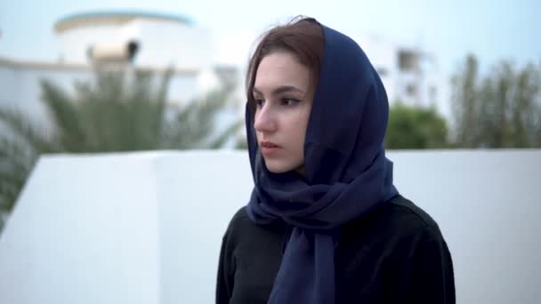 Wanita muda di arab headscarfl. Seorang wanita berjalan di sekitar halaman. Terhadap latar belakang rumah Arab . — Stok Video