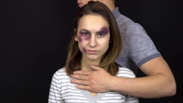 Un hombre joven abraza a una mujer joven. Una mujer con moretones en la cara. Pelea en una familia joven. Violencia doméstica. Sobre un fondo negro — Vídeos de Stock