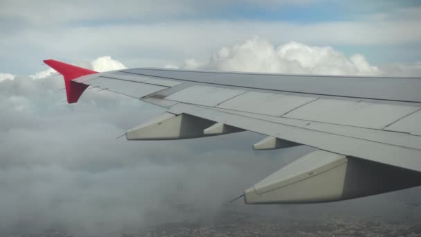 El avión vuela sobre la ciudad en nubes grises. Vista desde la ventana del avión hasta el ala — Vídeos de Stock