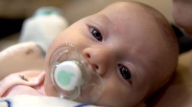 Annesinin kollarında bir bebek. Bir çocuk kuklayı emer ve kameraya bakar. Yüzünü kapat.