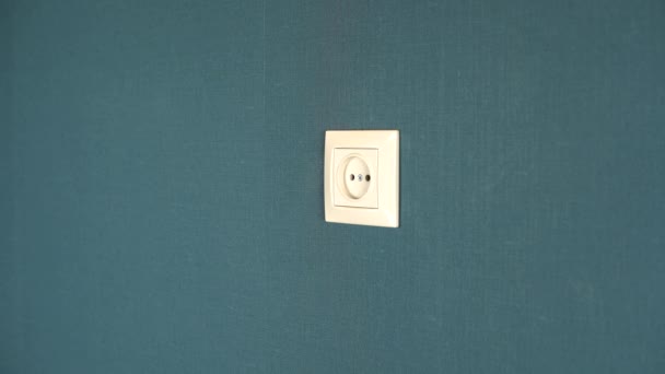 A man plugs a phone charger into a wall outlet. Rosette in the wall with dark blue wallpaper — Stock Video