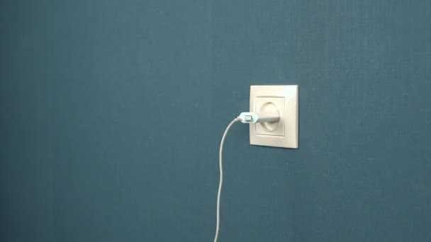 A man pulls out a phone charger from a wall outlet. Rosette in the wall with dark blue wallpaper — Stock Video