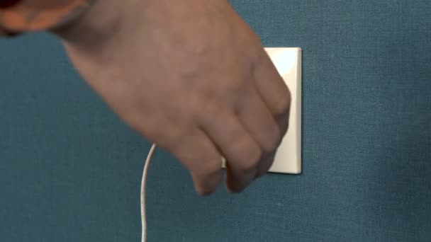 A man pulls out a phone charger from a wall outlet. Rosette in the wall with dark blue wallpaper. Closeup — Stock Video