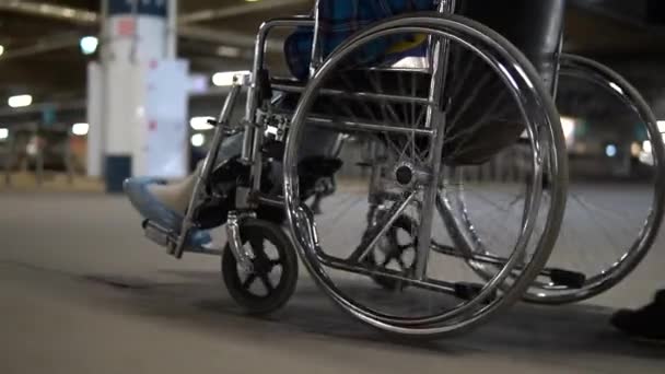 Rolstoel rijdt onderaanzicht. Een vrouw draagt een gehandicapte in een rolstoel. Wielen dicht — Stockvideo