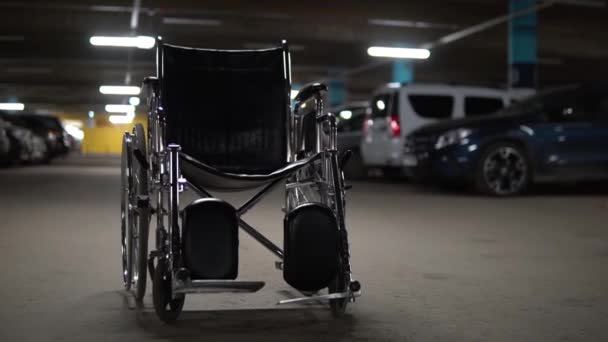 Een lege rolstoel staat midden in een parkeergarage. Rolstoel staat op de weg — Stockvideo