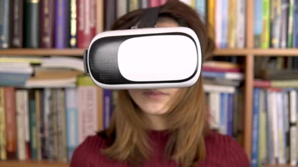 Une jeune femme lit un livre avec des lunettes BP à la bibliothèque. Une femme portant un casque VR sur la tête feuillette des pages de réalité virtuelle. En arrière-plan se trouvent des livres sur les étagères. Bibliothèque de livres . — Video