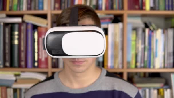 Een jongeman leest een boek met Vr-bril in de bibliotheek. Een man met een Vr helm op zijn hoofd bladert door pagina 's in virtual reality. Op de achtergrond staan boeken op boekenplanken. Boekenbibliotheek. — Stockvideo