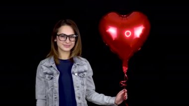 Genç bir kadın, kalp şeklinde şişme bir balonu öper. Siyah arka planda helyum dolu balonu olan bir kadın. Sevgililer Günü tüm sevgililerin günüdür..