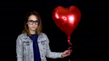 Üzgün genç kadın kalp şeklindeki balonu bıraktı. Üzgün bir kadın siyah arka planda helyum topları ile duruyor. Sevgililer Günü tüm sevgililerin günüdür..