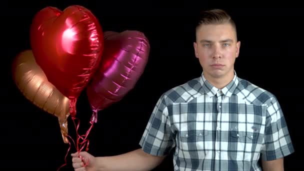 Trauriger junger Mann ließ herzförmige Luftballons los. Ein trauriger Mann steht mit Heliumkugeln auf schwarzem Grund. Valentinstag ist der Tag aller Verliebten. — Stockvideo