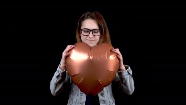 Una joven enojada rompió un globo en forma de corazón. Mujer enojada sobre un fondo negro. Día de San Valentín es el día de todos los amantes . — Vídeos de Stock