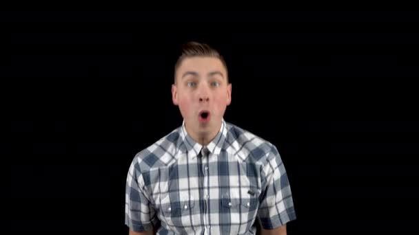De jongeman toont emoties van verbazing op zijn gezicht. Verrast man in een shirt op een zwarte achtergrond. — Stockvideo