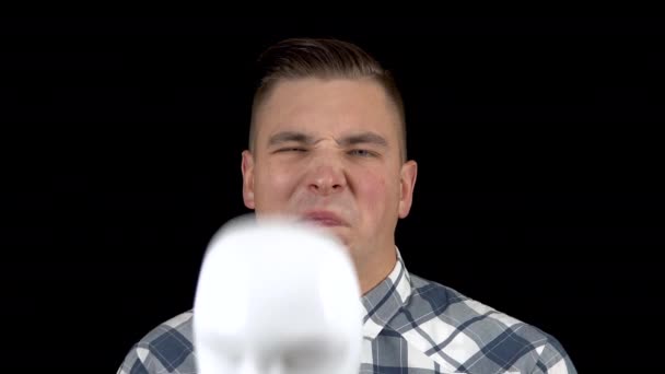 A young man takes off his mask and shows an emotion of disgust on his face. The man is unpleasant. A man hides his face behind a white mask on a black background closeup — Stock Video