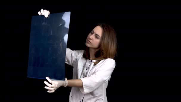 A young woman doctor checks the results of an MRI scan of a spine. A woman examines an MRI image then shows a thumb up. Positive MRI result. On a black background. — 비디오