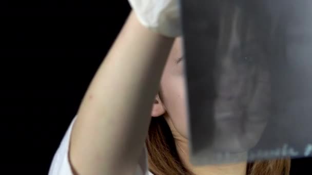 Young woman doctor checks the results of an x-ray of the foot. A girl is considering a close-up x-ray. On a black background. View through an x-ray image. — 비디오