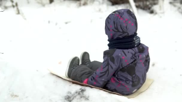 A child rolls on a snow slide. Winter fun on the street. In the cold winter, the child is dressed in a jacket with a scarf. Side view. Slow motion — Stock Video