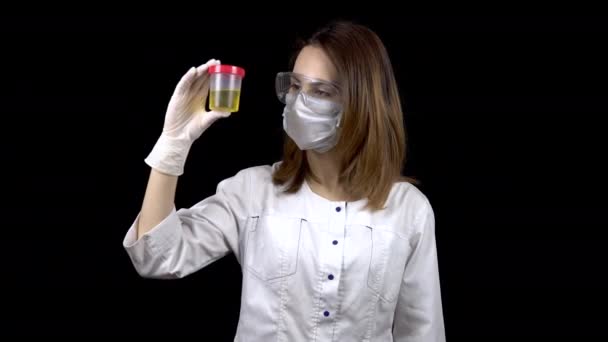 La jeune femme médecin vérifie les analyses d'urine. Une femme examine un bocal de test, puis montre un pouce vers le haut. Test d'urine positif. Sur fond noir — Video