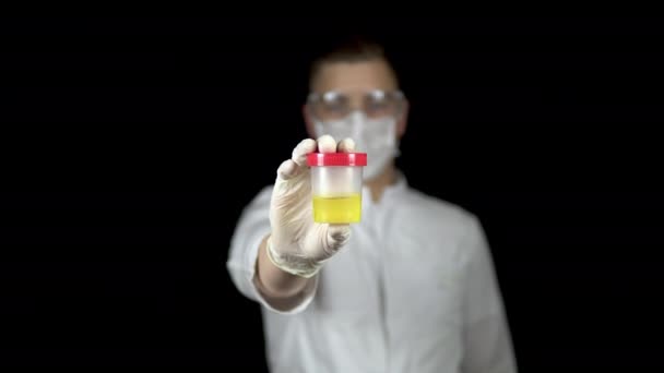 Urine in een testbank close-up. Man arts houdt een blik urine naar de camera op een zwarte achtergrond. — Stockvideo