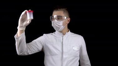 Genç doktor sperm testlerini kontrol ediyor. Adam test kavanozunu inceliyor, sonra baş parmağını aşağı gösteriyor. Sperm analizi negatif. Siyah bir arkaplanda.
