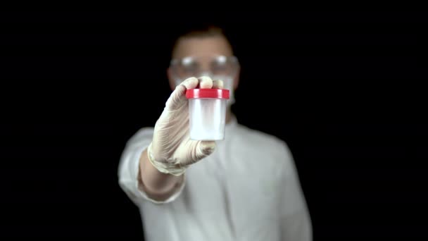 Esperma em um banco de testes close-up. Homem médico segura um frasco de esperma para a câmera em um fundo preto . — Vídeo de Stock