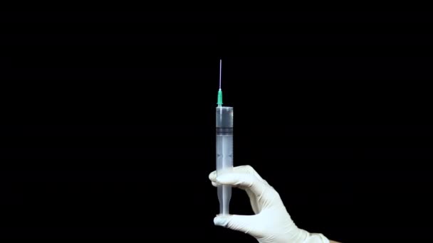 Seringue avec le gros plan du médicament. Le médecin saupoudre de la seringue pour libérer l'air. Le médecin tient une seringue dans un gant sur un fond noir .