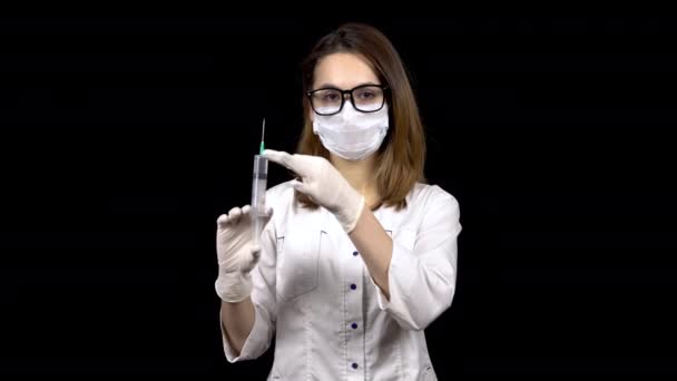 Young woman doctor is standing with a syringe filled with medication. A doctor sprays from a syringe to release air on a black background. — 비디오