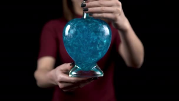 Una giovane donna offre una bottiglia con una pozione d'amore nella fotocamera. Bottiglia di vetro a forma di cuore con liquido blu. San Valentino è il giorno di tutti gli amanti. — Video Stock