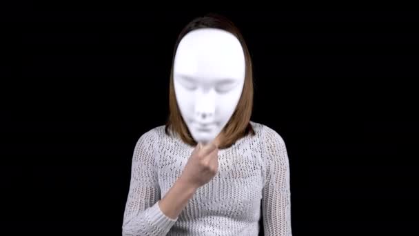 Молодая женщина снимает маску и показывает эмоции гнева на своем лице. Женщина кричит, стоя на черном фоне. Девушка прячет лицо за белой маской. — стоковое видео