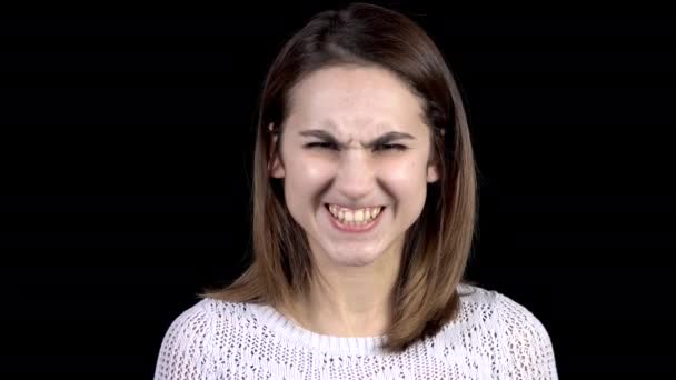 De jonge vrouw toont emoties van woede op zijn gezicht. Meisje grijnst tanden en fronst wenkbrauwen op een zwarte achtergrond closeup. — Stockvideo