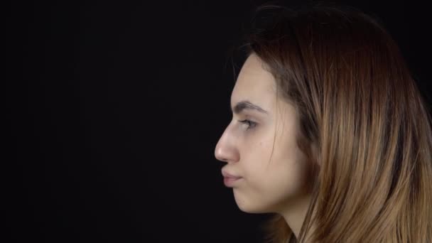 A fiatal nő aktívan rázza a fejét. Egy nő forgatja a fejét, és az ajkai remegnek egy fekete háttér közeli felvételen. Lassú mozgás.. — Stock videók