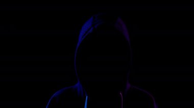 A young woman is standing in the hood hiding her face. An attacker is standing in the dark. Blue and red light falls on the person on a black background.