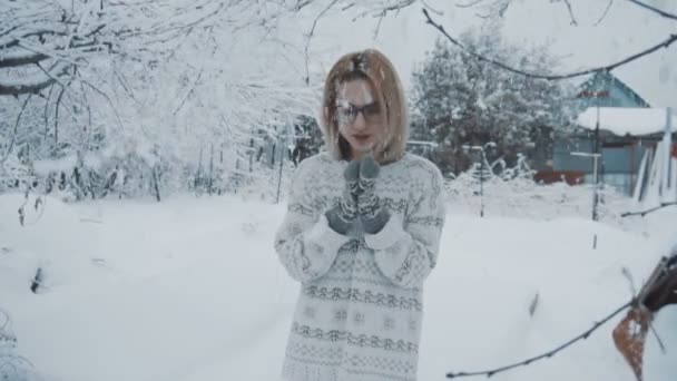 La fille en lunettes, dans un pull et mitaines se tient dans la rue sous la neige en hiver lent — Video