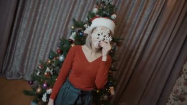 Kırmızılı kız elinde bir kar tanesiyle Noel ağacının arkasında duruyor. Noel şapkalı kız.