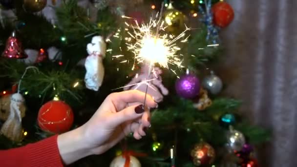 Una chica sostiene una chispa contra el fondo del árbol de Navidad lento — Vídeo de stock