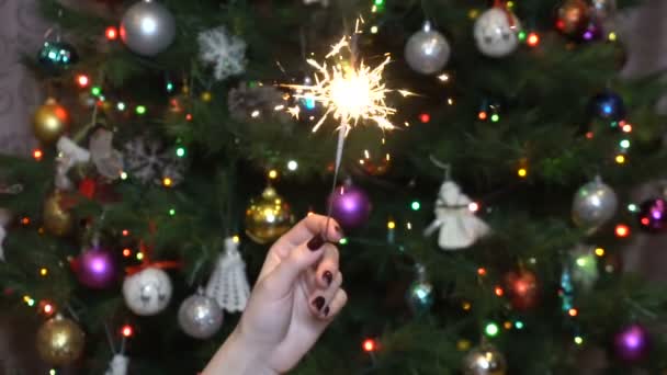 Una chica sostiene una chispa contra el fondo del árbol de Navidad lento — Vídeo de stock