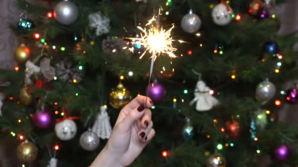 Dívka drží jiskru na pozadí vánočního stromečku pomalu
