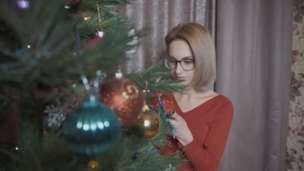 Το κορίτσι με τα κόκκινα θαυμάζει το χριστουγεννιάτικο δέντρο. Εξετάζει παιχνίδια — Αρχείο Βίντεο