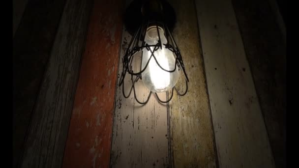 Vieille ampoule brille dans l'obscurité sur les panneaux de couleur de fond — Video